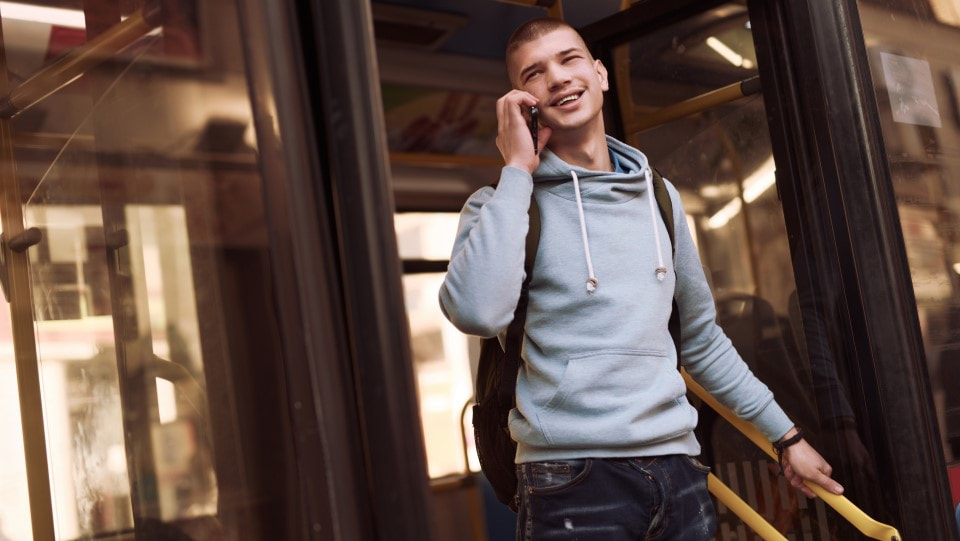 Young man gets off the bus while using his phone to walk and talk